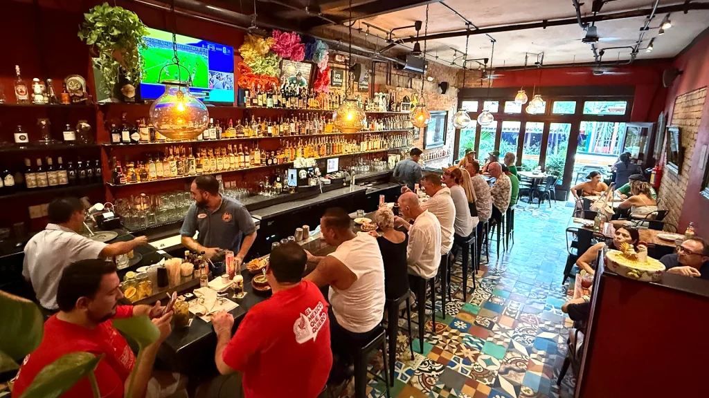Interior of Joe Jack's Fish Shack in Puerto Vallarta with guests dining at a long bar, colorful tile floors and pendant lighting.