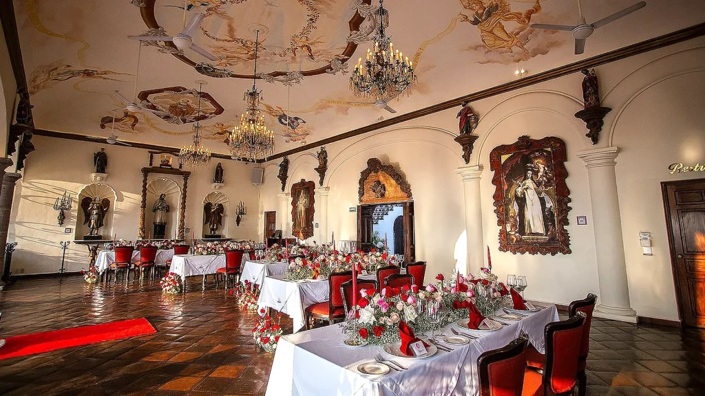 Elegant dining room at La Cappella Italian restaurant in Puerto Vallarta with ornate chandeliers, painted ceiling frescoes, red chairs and floral arrangements.