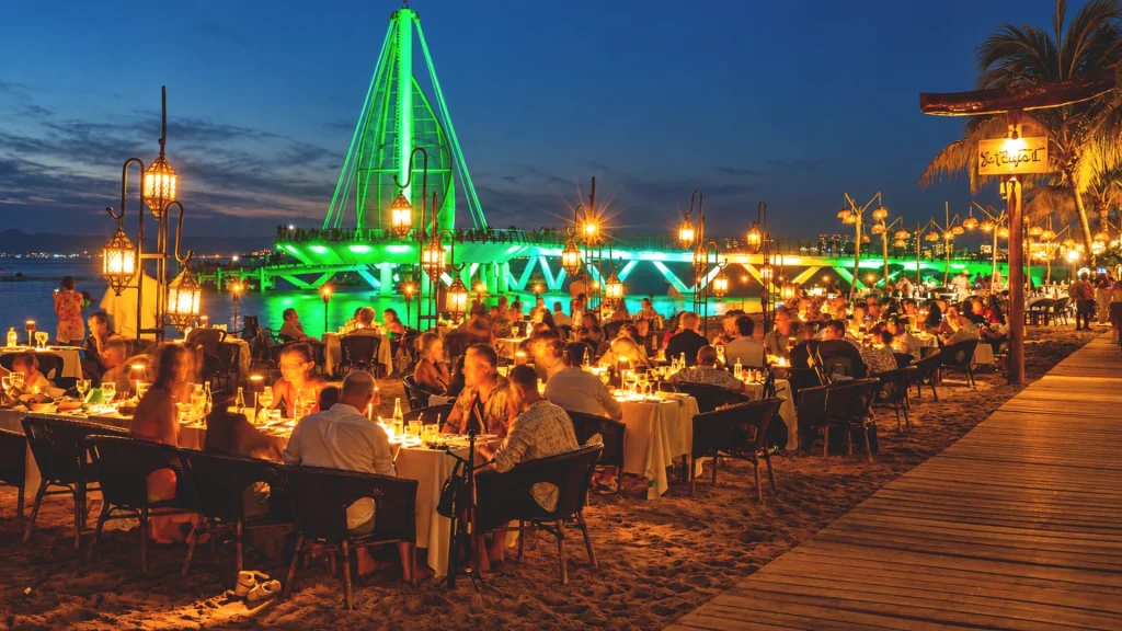 Candlelit beachfront dining at La Palapa Restaurant in Puerto Vallarta, with the illuminated Los Muertos Pier overlooking the ocean at dusk.