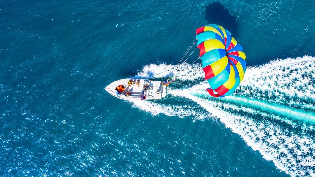 Aerial view of a colorful red, yellow and blue parasail towed by a white motorboat across the blue waters of Banderas Bay near Nuevo Vallarta.