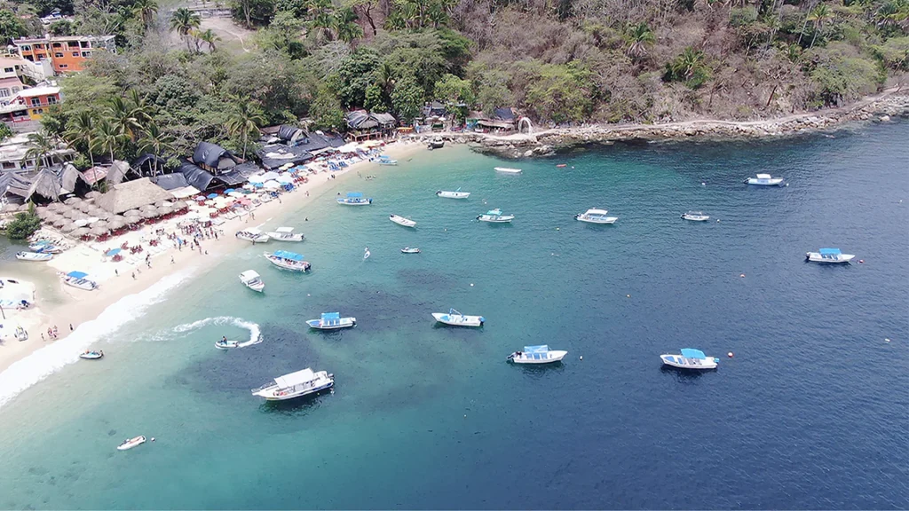 Aerial view of Playa Mismaloya with turquoise water, anchored boats, and tropical coastline near Puerto Vallarta, Mexico.