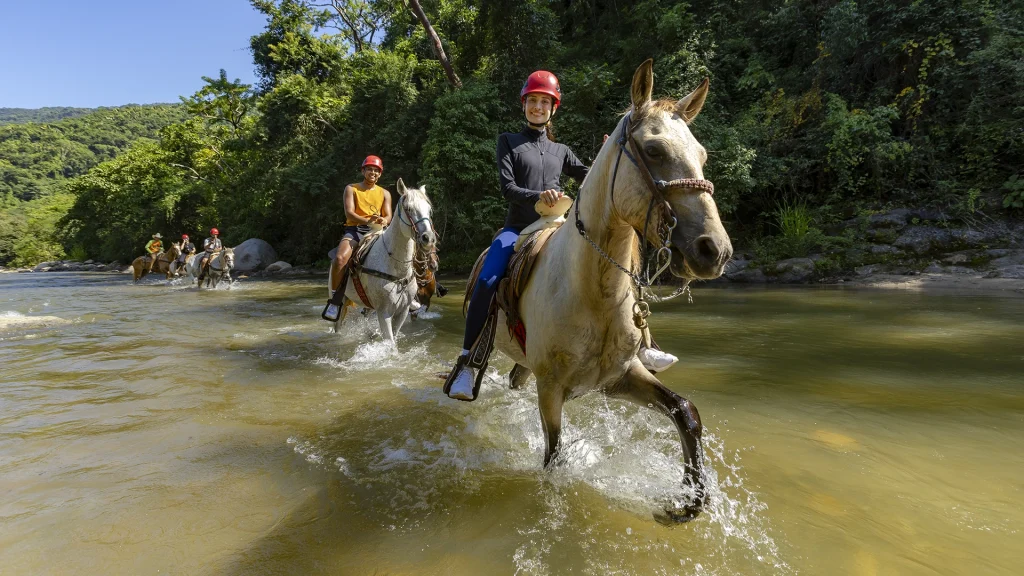 Guests horseback riding through a river in the Sierra Madre during the River Park tour near Puerto Vallarta