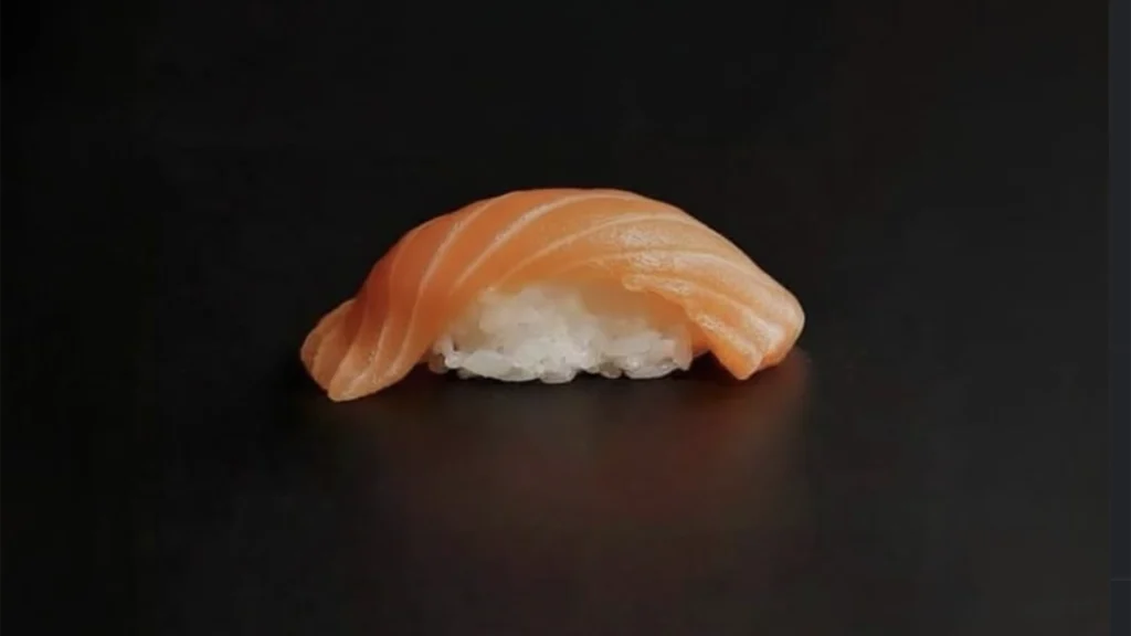 Fresh salmon nigiri sushi with thin slices of orange salmon over white sushi rice against a black background at Satori Sushi in Puerto Vallarta.