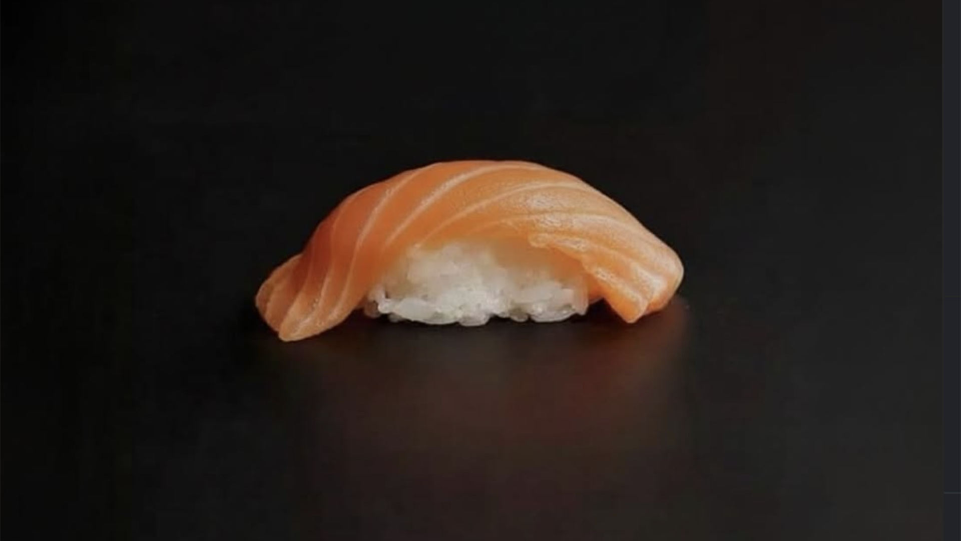 Fresh salmon nigiri sushi with thin slices of orange salmon over white sushi rice against a black background at Satori Sushi in Puerto Vallarta.